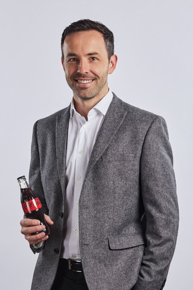 Oliver Crick, group commercial development director, CCEP stands drinking a bottle of Coke