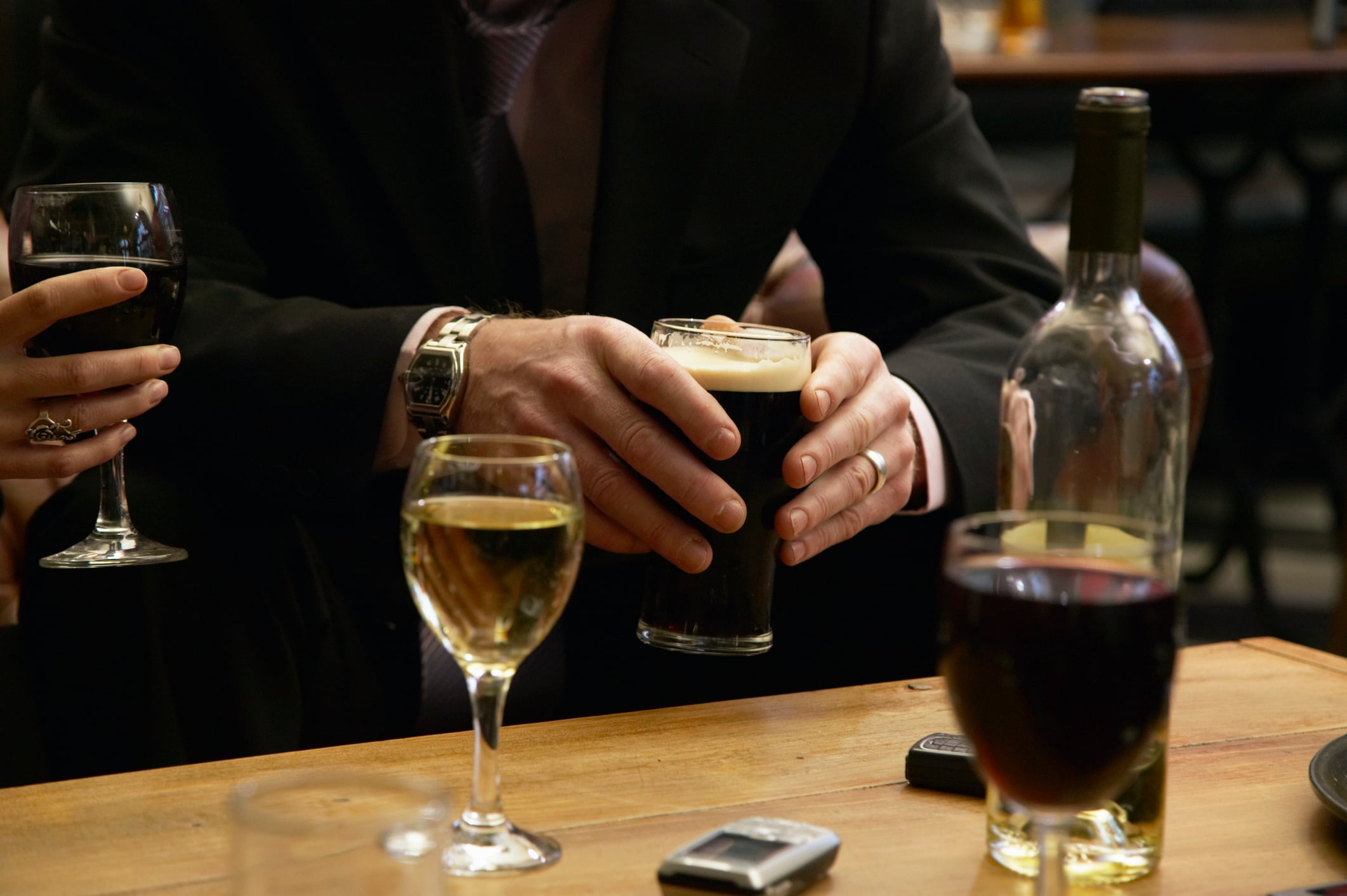 Businessman sitting in bar holding drink, mid section.