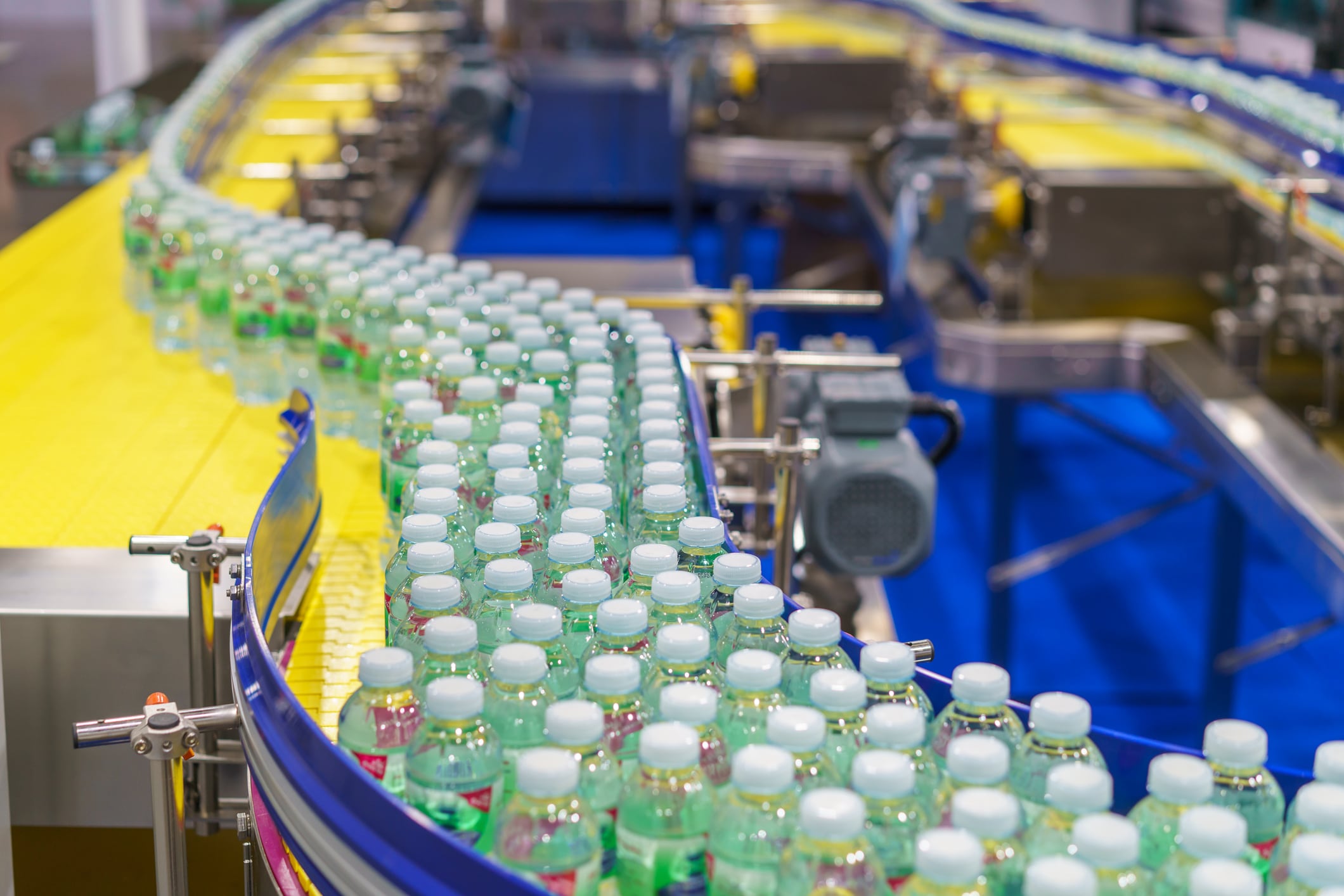 Hundreds of clear plastic bottles filled with fresh drinking water moving along a curved conveyor belt on an automated production line inside a modern beverage manufacturing plant.