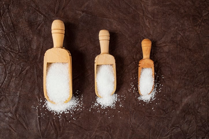 Three wooden scoops in different sizes full of white crystal sugar on brown leather background, sweets portion   concept