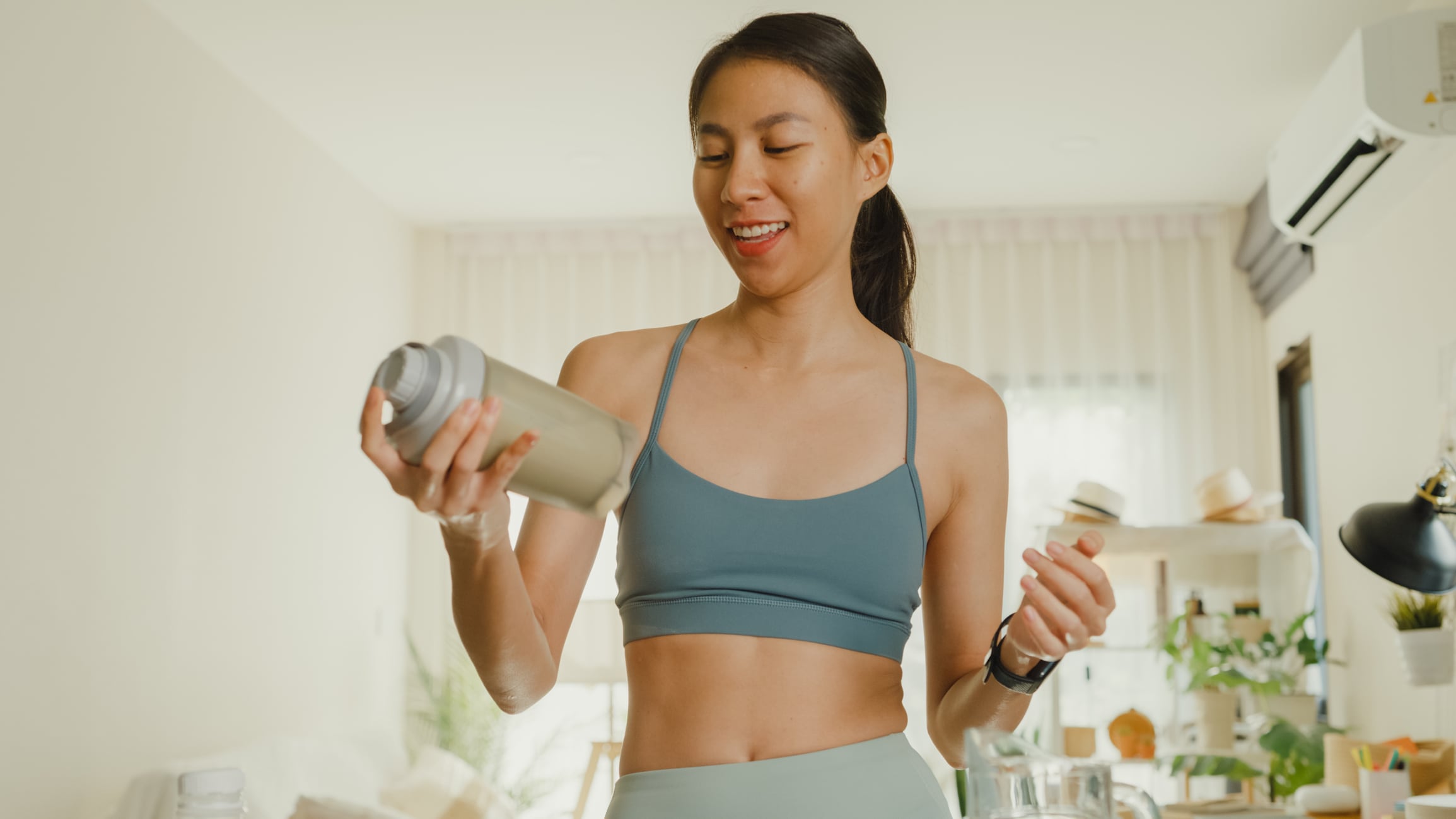 Young Asian athletic woman preparing protein shake at home. Diet and healthy food concept.