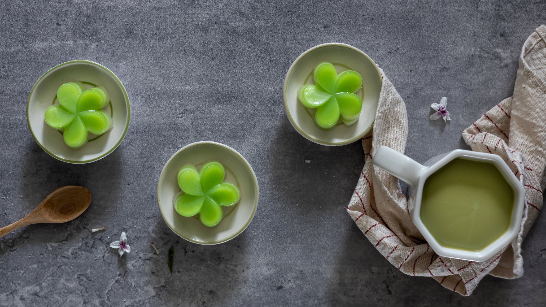 Top view of a steamed pandan layer cake on small cups, served with a cup of green tea, a traditional Thai dessert. Close-up. Flat lay.