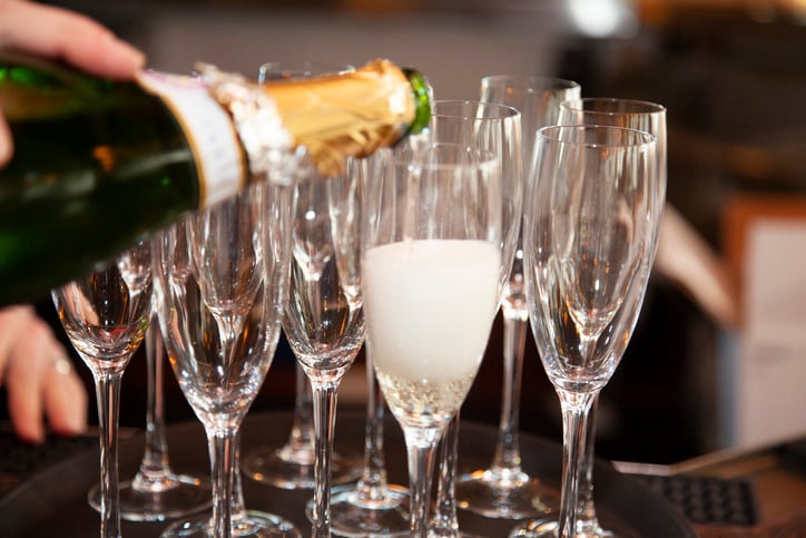 filling a champagne glass with champagne that has lots of bubbles. Many glasses are sitting behind the glass that is being filled