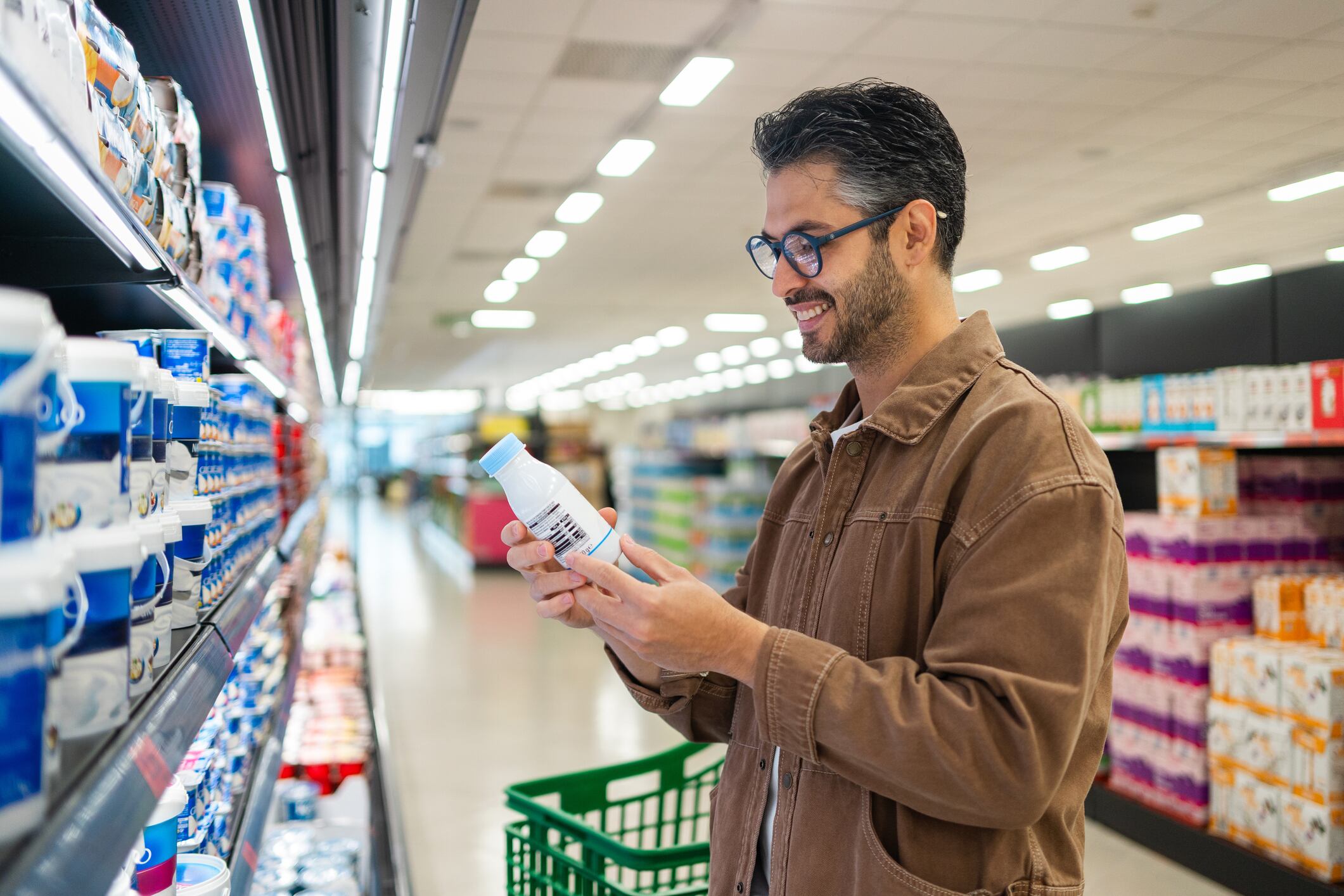 Young adult man smiling while carefully checking nutritional information on a dairy product in a grocery store