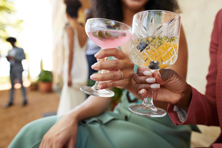 Midsection of female guests toasting alcoholic drinks sitting together at wedding party