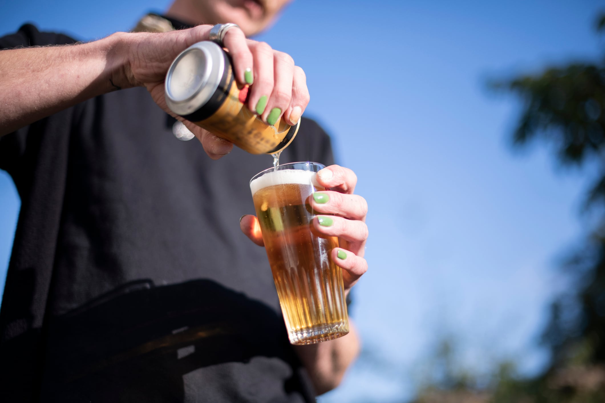 Person emptying a beer can in their glass, outdoors in the sun