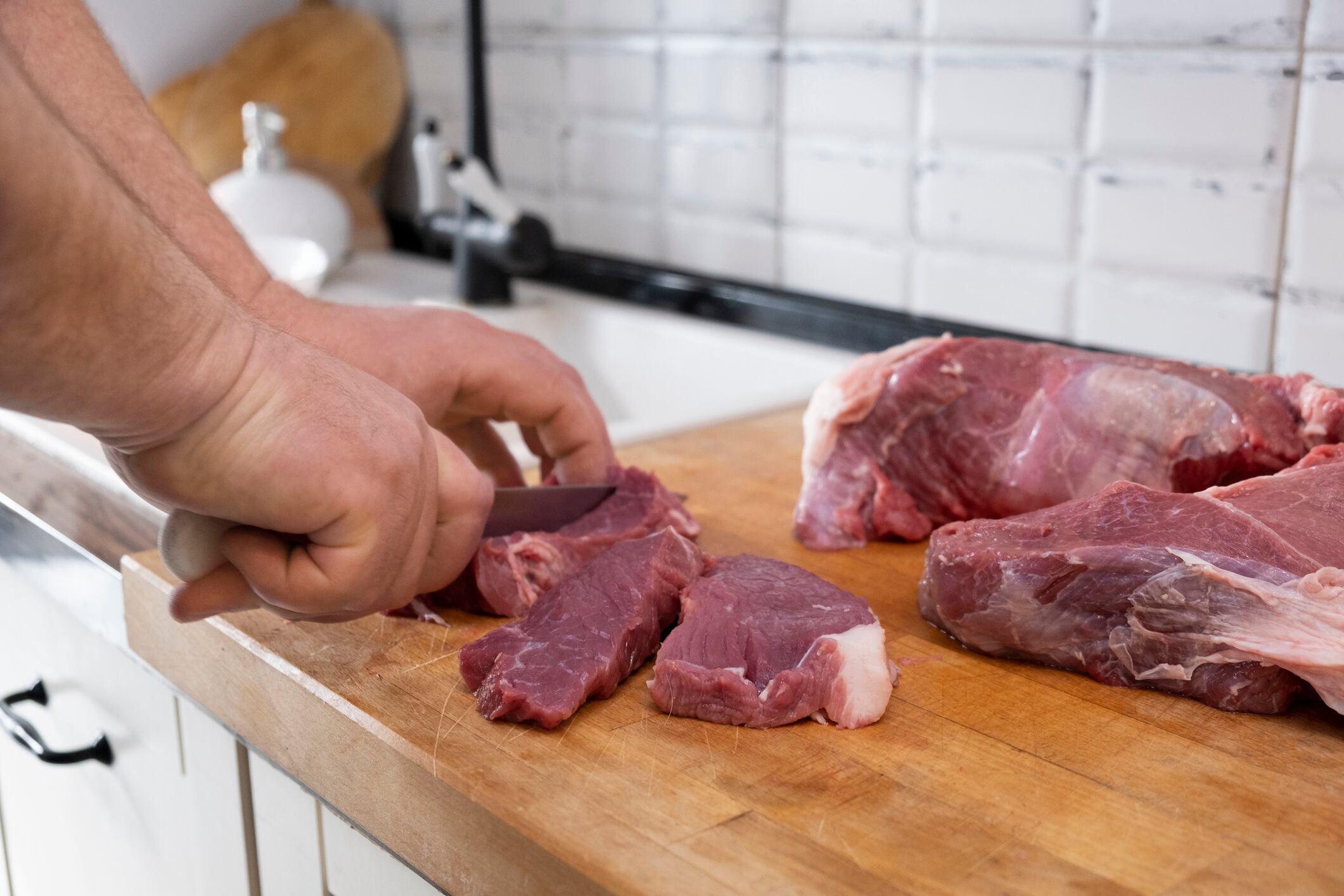 Man cutting fresh raw meat on  board in white kitchen. Preparing pork meat, cooking.