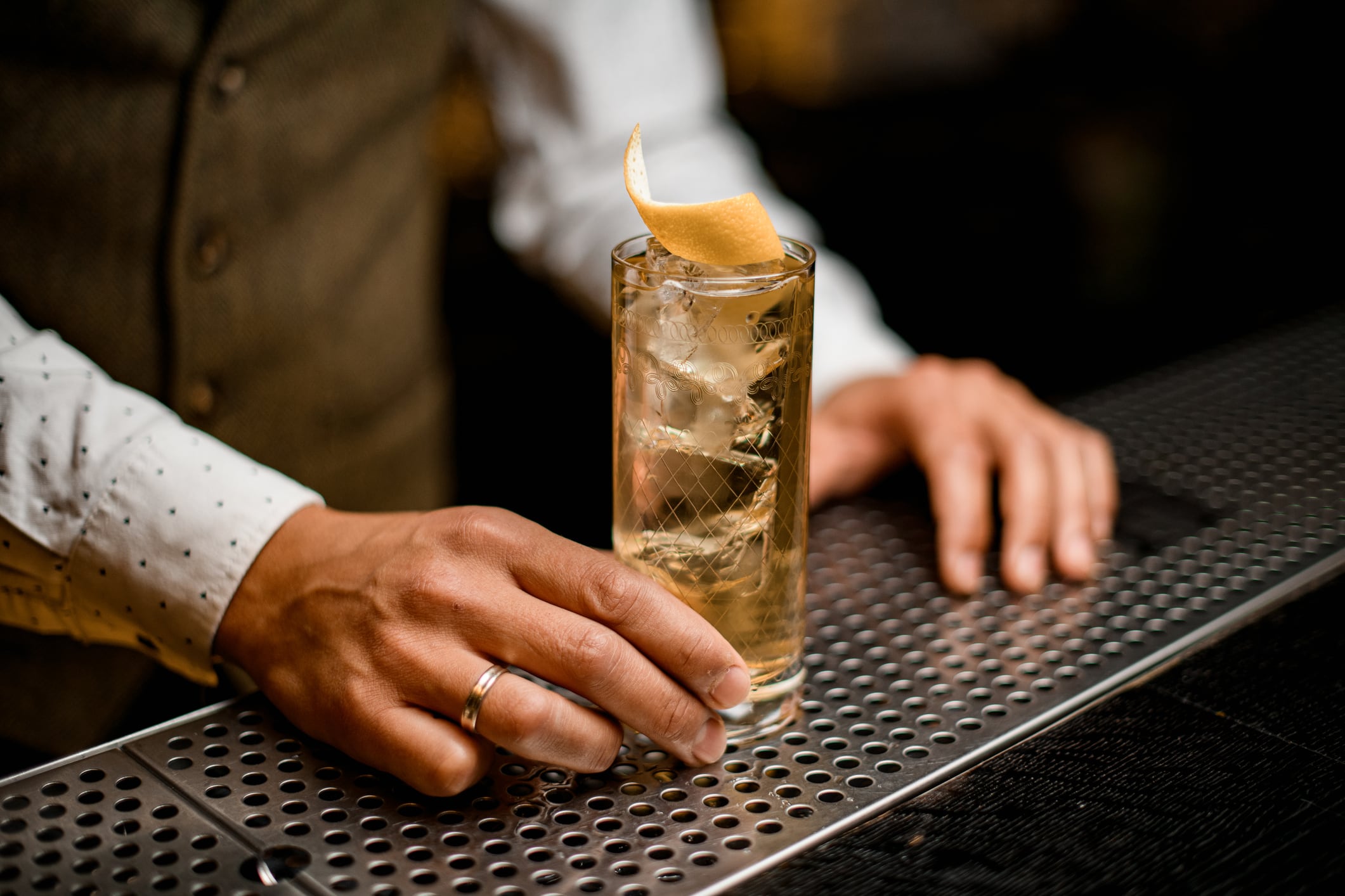 great view on crystal glass with refreshing cold iced drink decorated with citrus peel and bartender's hand on bar counter