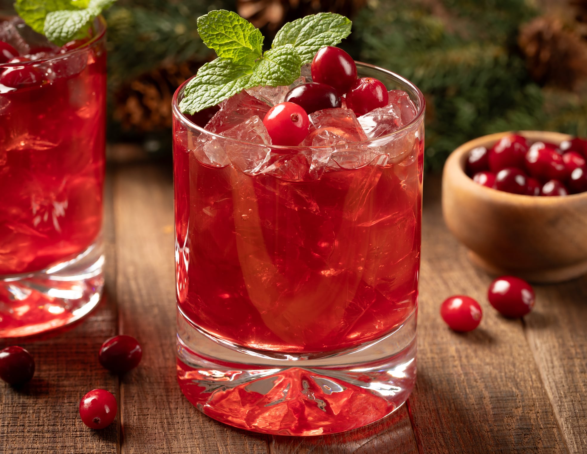 Cranberry drink with fresh cranberries and mint leaves on wooden surface.