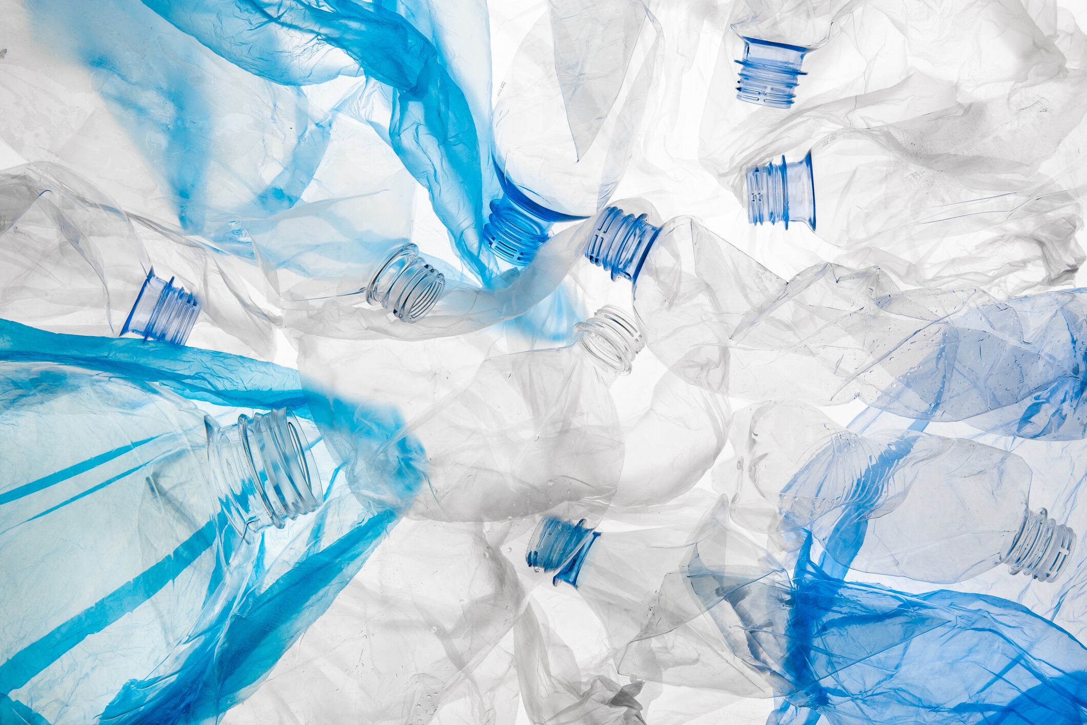 Empty twisted used backlit blue plastic bottles and wrinkled bags pattern on white background isolated. Environment pollution conceptual poster, banner template.