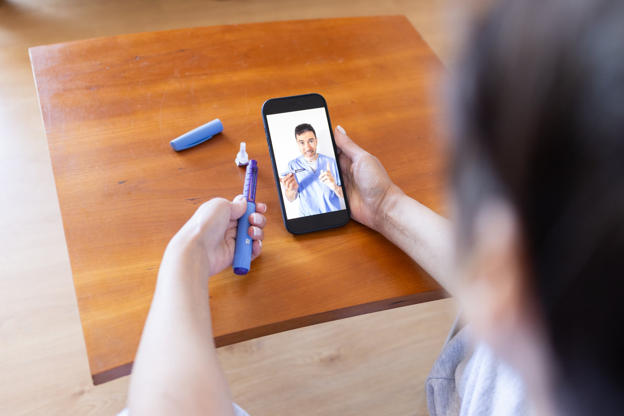Patient is holding a semaglutide pen injector while having a video call with a doctor on a smartphone, receiving instructions on how to administer the medication for weight loss and obesity