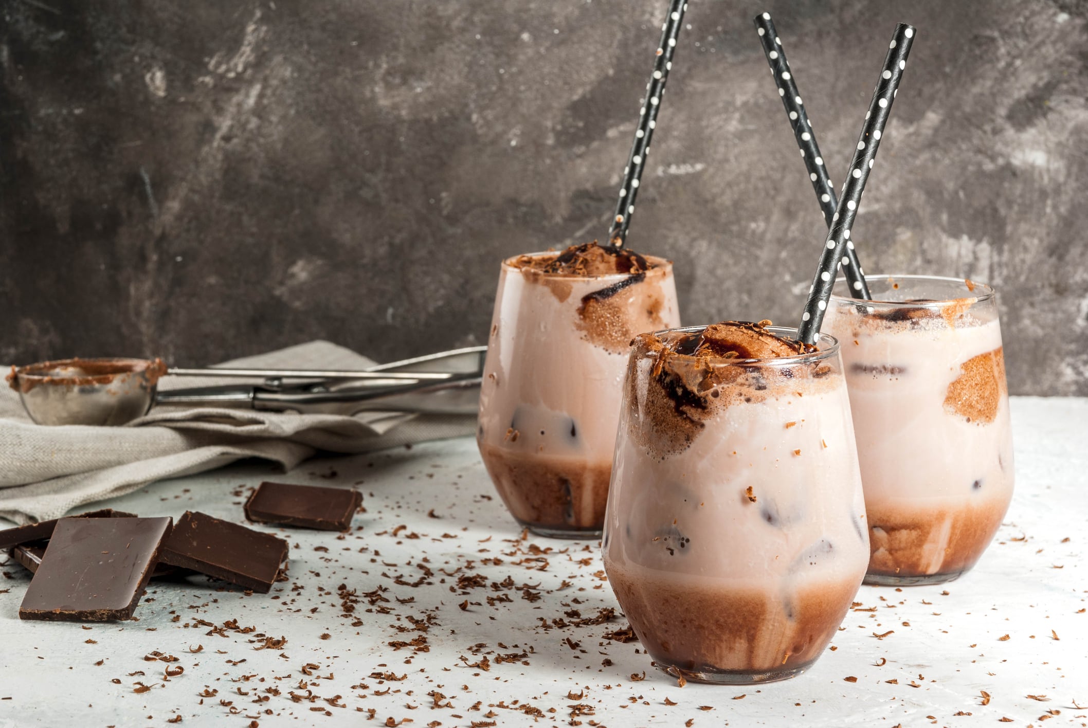 Summer refreshment drinks. Chilled iced chocolate cocoa. With scoop of chocolate ice cream, chocolate powder and ice. In glasses, with tubes for drinking. White concrete table. Copy space