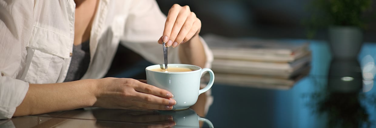 Happy woman stirring coffee sitting in the living room in the night at home