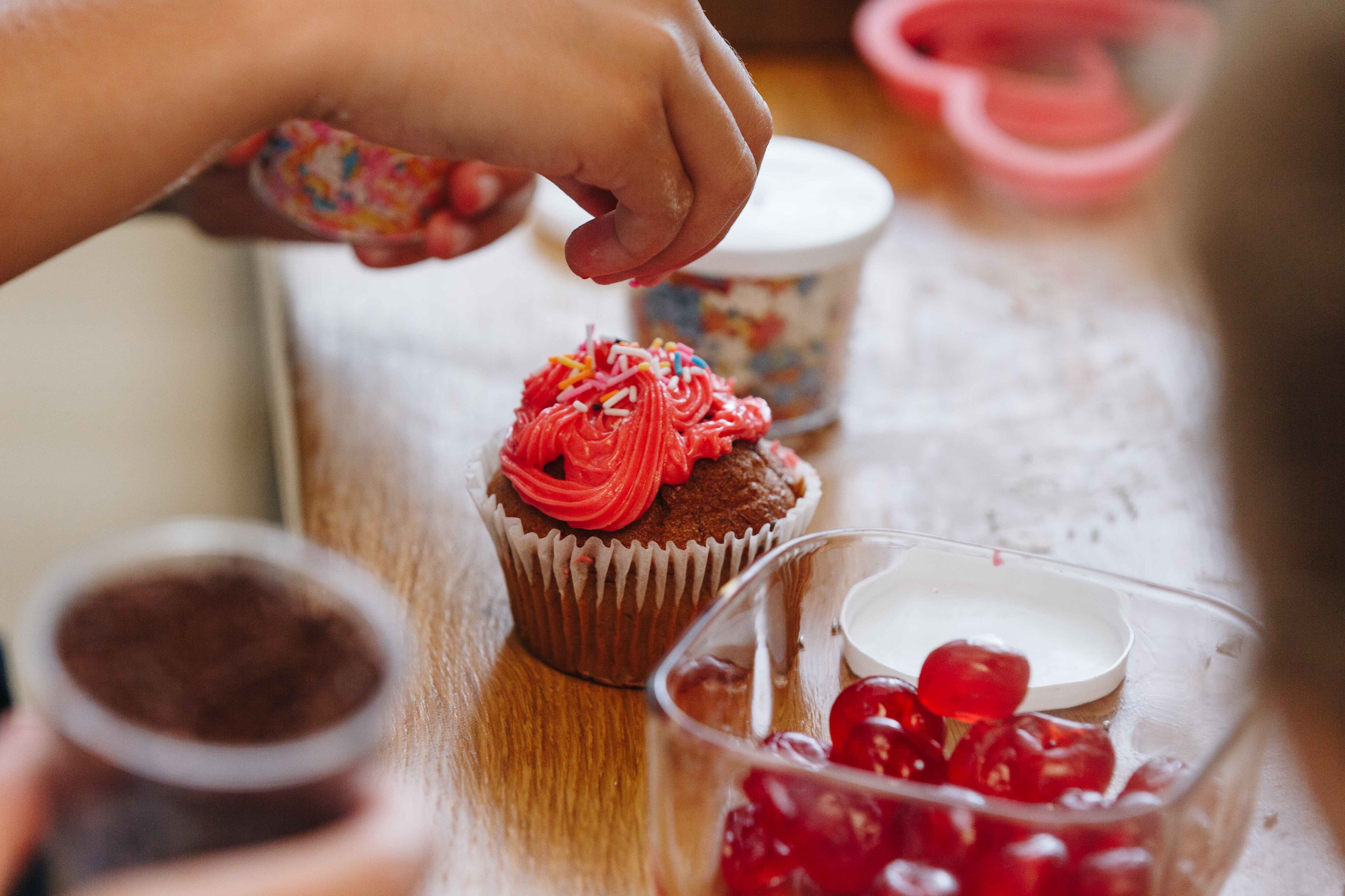 Child decorating cupcake with red frosting