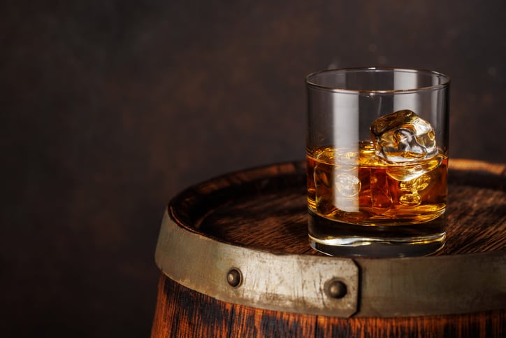 A classic whiskey glass filled with golden amber whiskey, placed on a wooden barrel