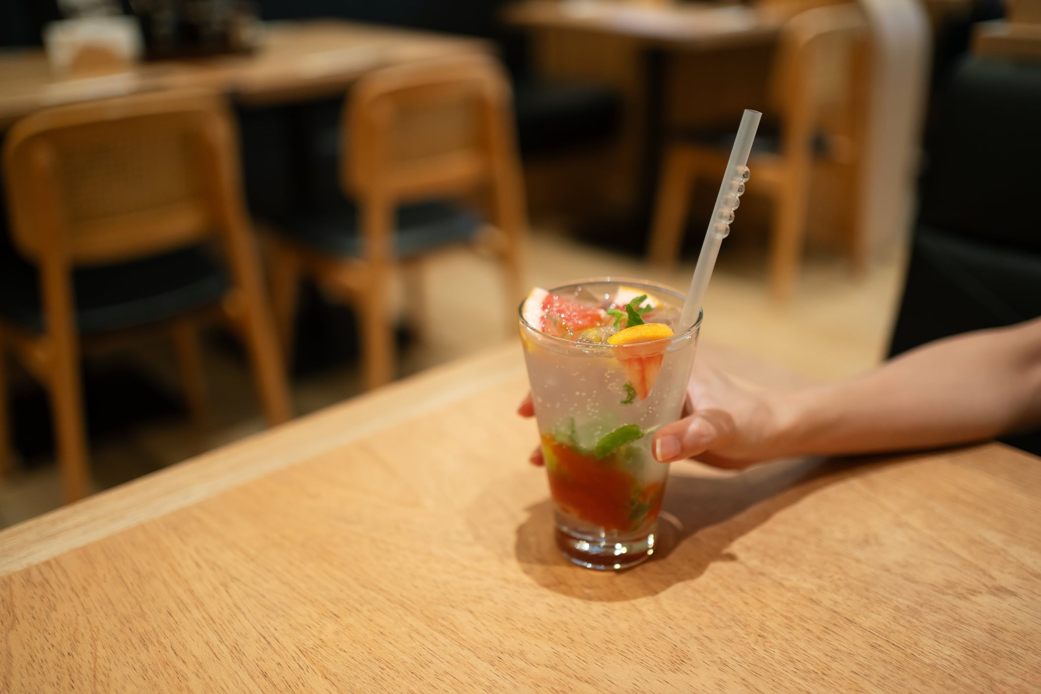 Hand holding cup of grapefruit and yuzu sparkling juice with fresh fruits and mint leaves.