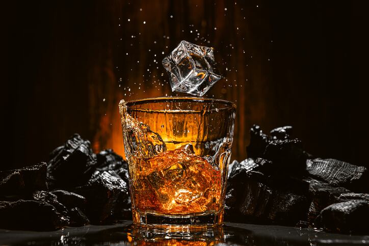 ice falls into a glass with expensive whiskey and spray flies in different directions
