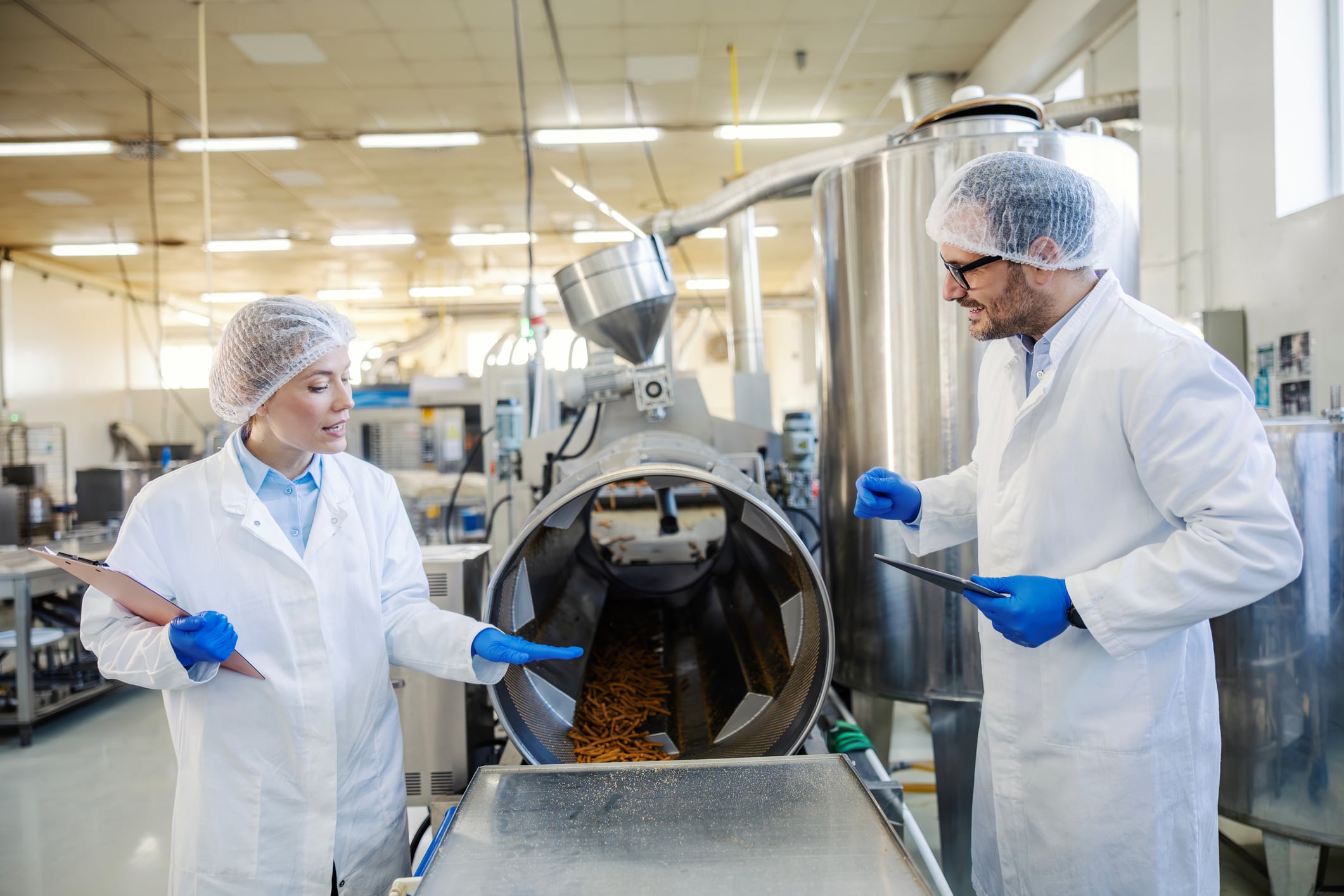 Two quality control workers overseeing manufacturing process, ensuring hygiene and standards in an industrial food production facility