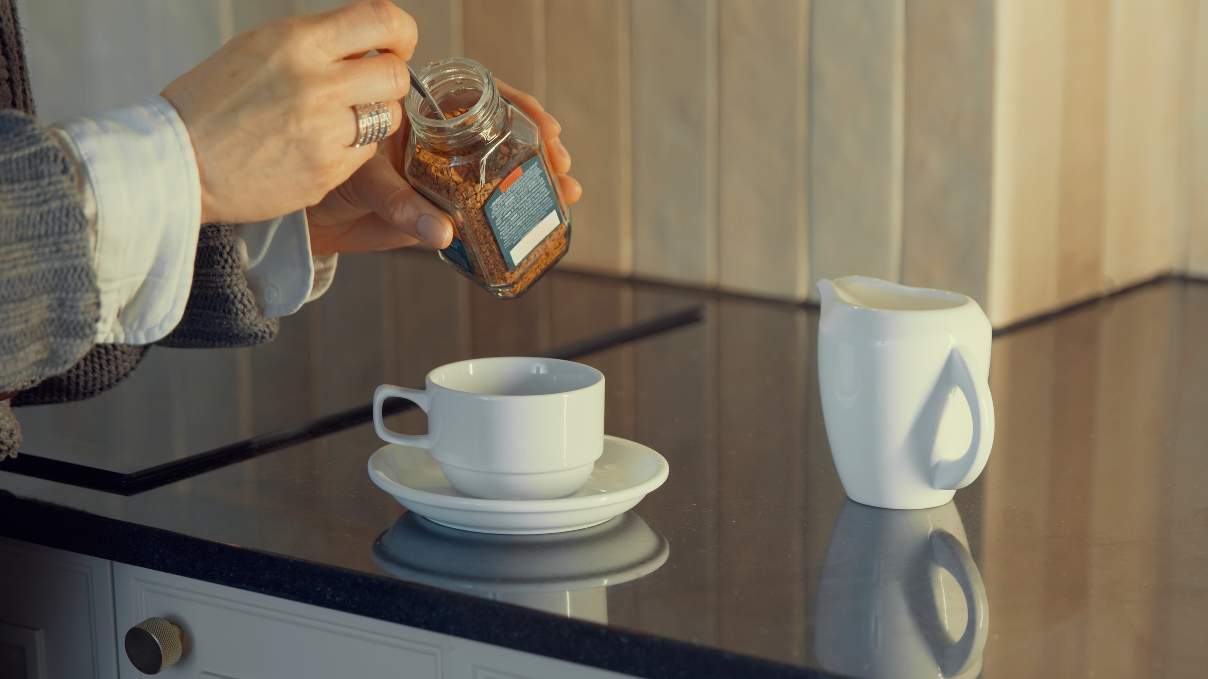 Person scooping instant coffee granules into a mug on a kitchen counter