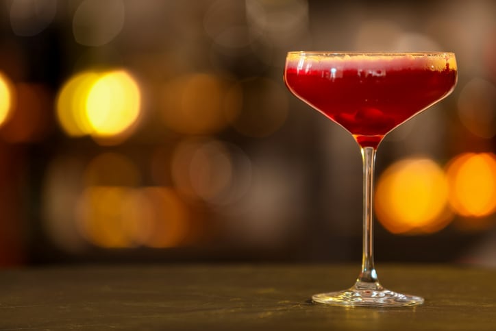 Glass of alcoholic cocktail on table against blurred background. Space for text