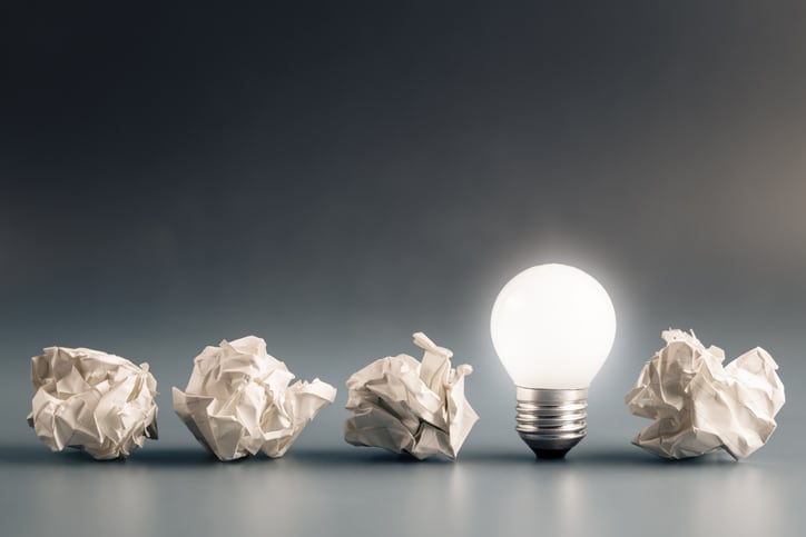 Small light bulb glowing in a row of crumpled paper balls, inspiration, problem and solution concept