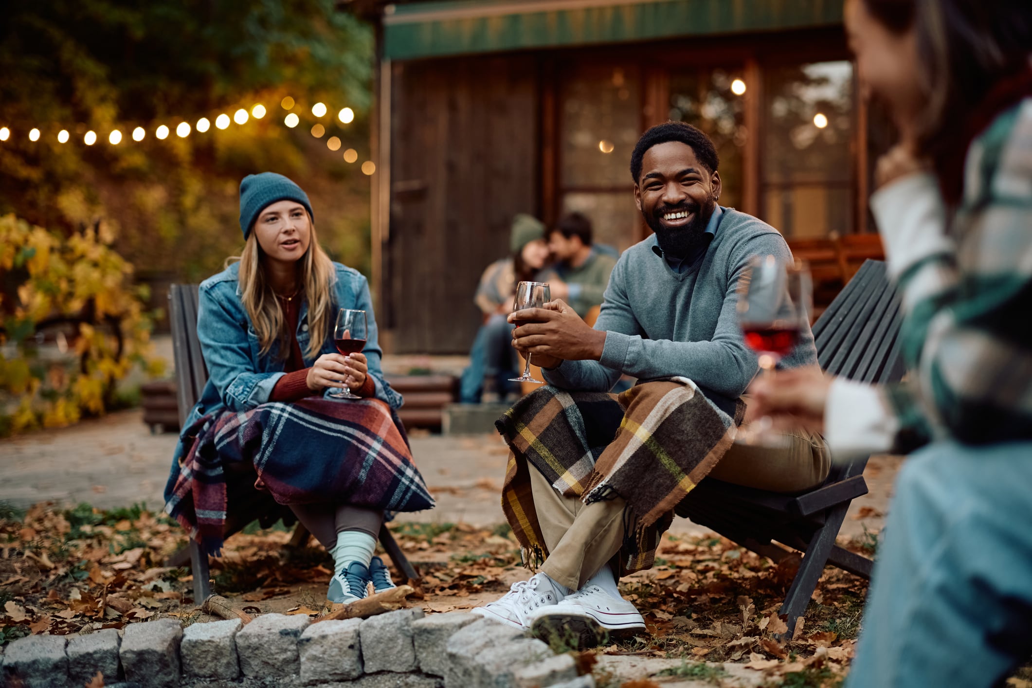Happy African American man talking to his friends while having a glass of wine in autumn.
