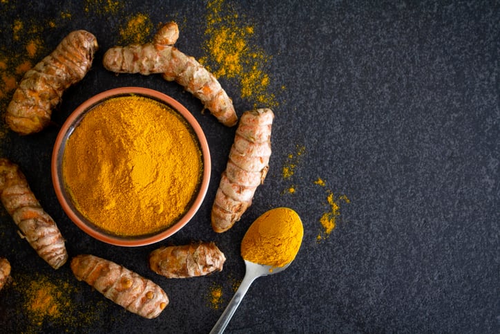 Fresh turmeric root and the powder spice in a small brown dish, on a dark gray slate background. Top view.
Flat lay with copy space to the right of the image.
Stock photo.