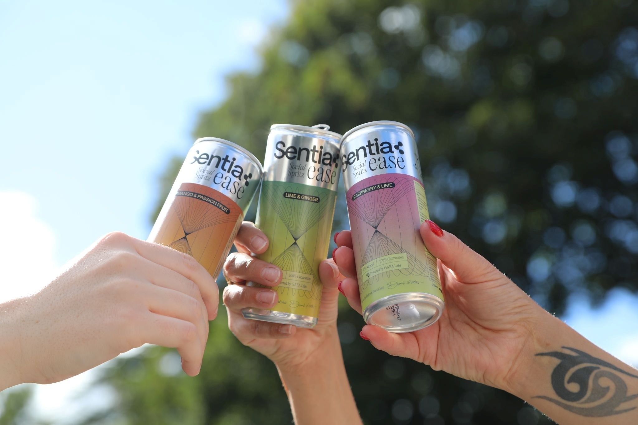 Three hands holding cans of Sentia Ease drinks outdoors against a sunny, leafy background.