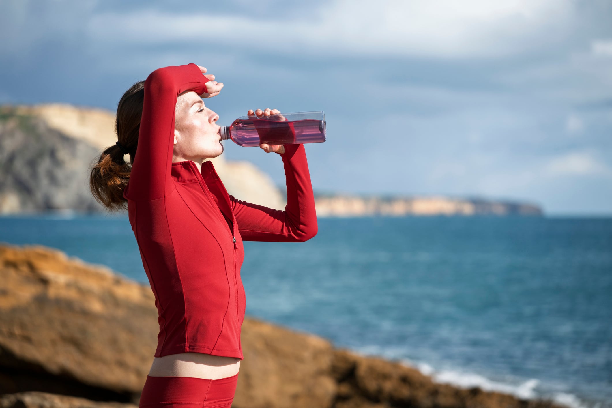 sporty woman drinking on cliffs by the sea after exercise