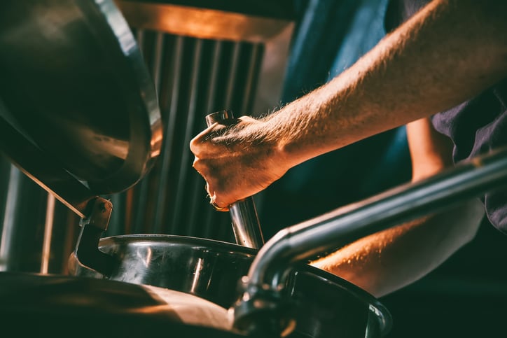 One male worker checking the brew from a machine.