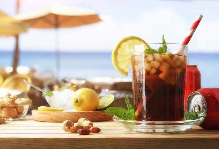 Cola in a glass with ice and lemon on a wooden table with canned fruit and appetizers on a bar by the sea. Front view.