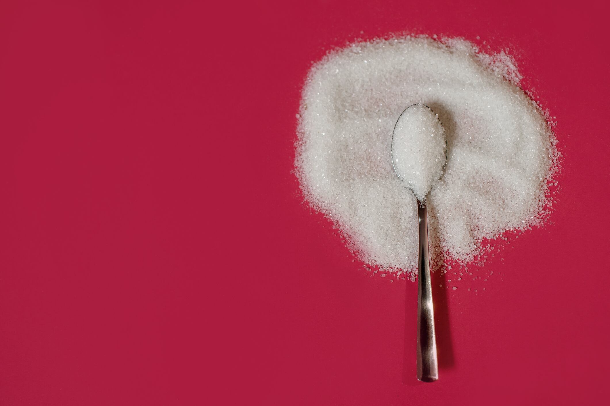 Powdered sugar on a red background with a metal spoon, top view, place for text, harm or benefit from white sugar