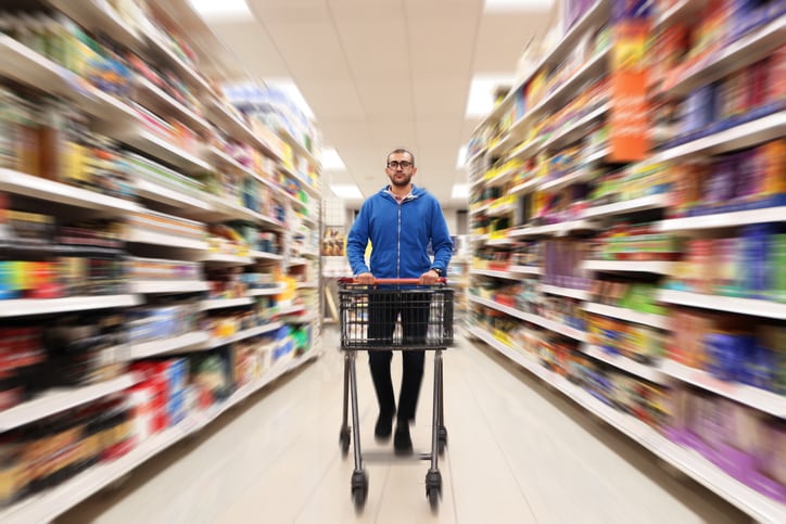 mixed race man walking quickly with trolley down aisle in supermarket or store