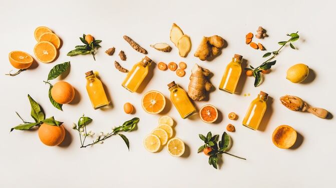Immune boosting natural vitamin health defending drink to resist virus. Flat-lay of fresh turmeric, ginger and citrus juice shots over white background, top view. Vegan Immunity system booster