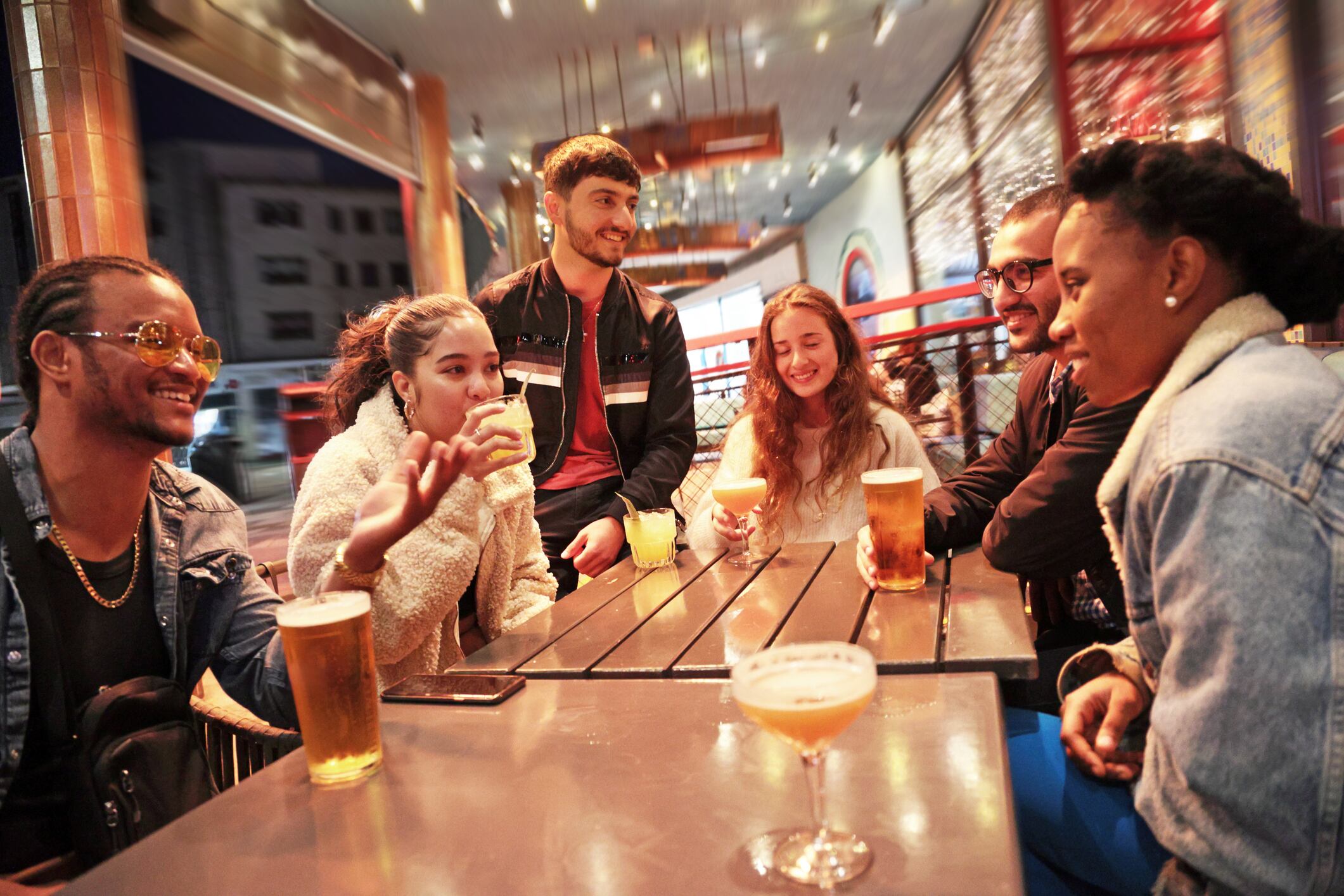 Mixed race group having a drink outside a bar at night. Laughing and having fun