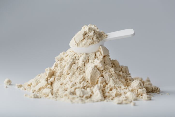 A mountain of  protein in powder with a measuring spoon on a white background.