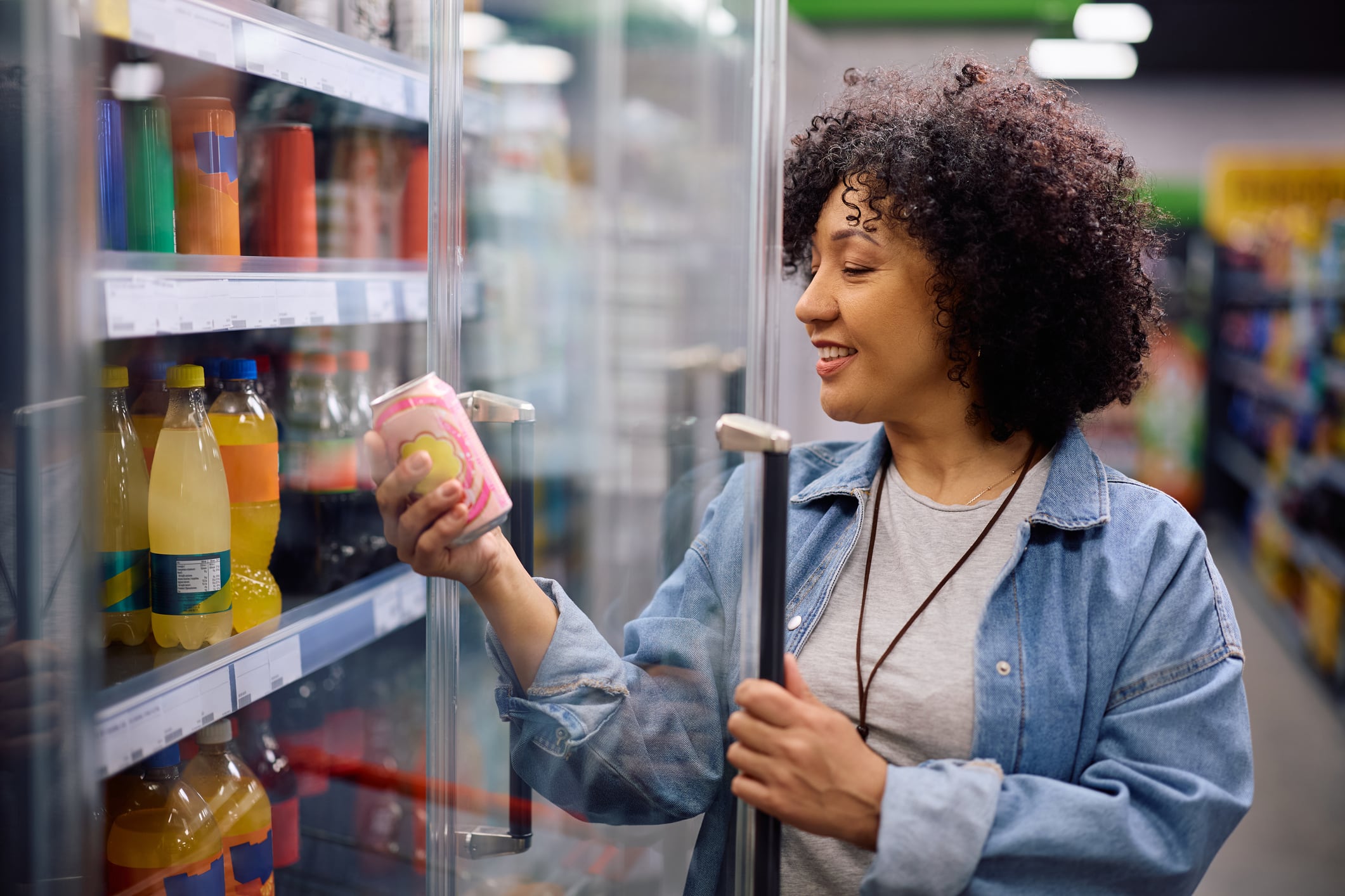 Happy mature woman buying cooled soda at the supermarket.