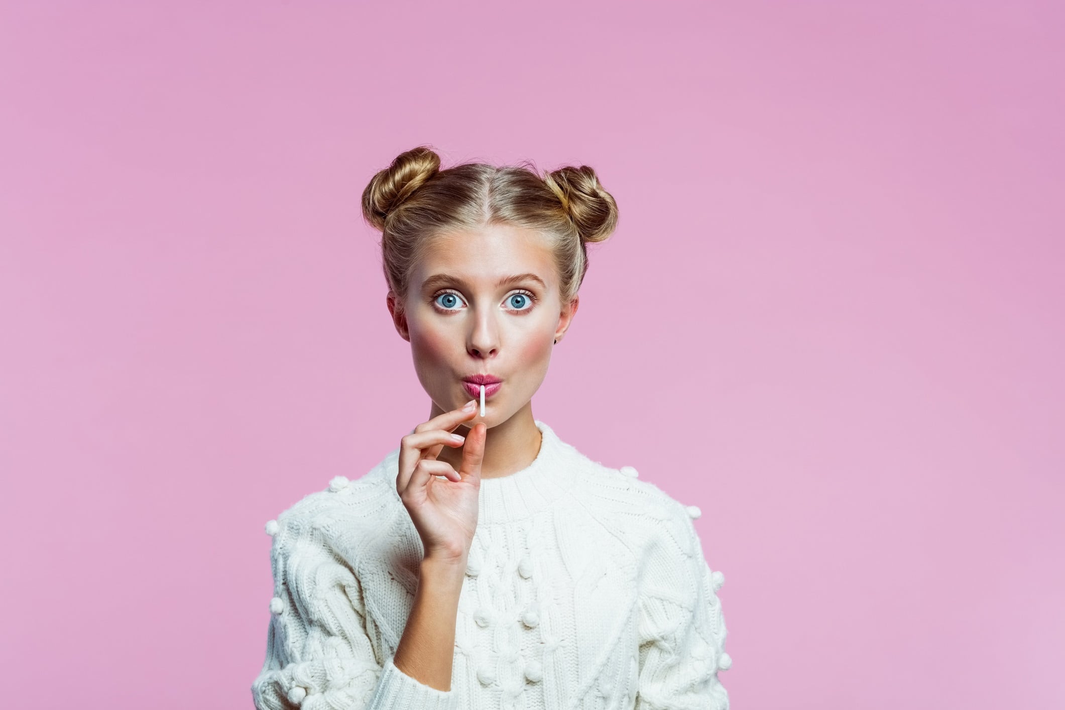Portrait of girl with hair in buns, wearing white top and holding a lollipop.