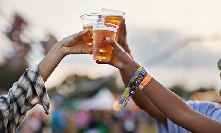 Hands of man and women toasting beer at music festival against sky at sunset