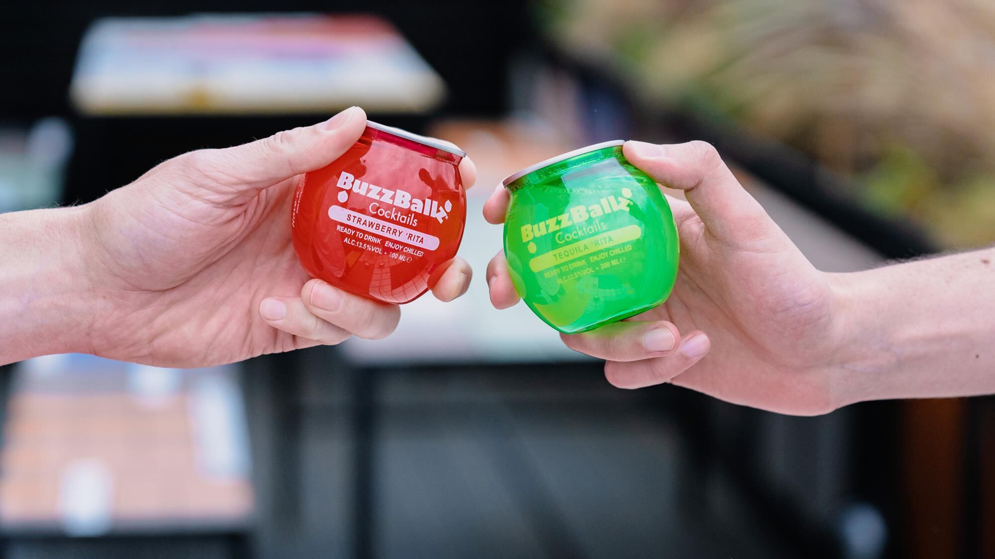 Two people cheers-ing with BuzzBallz RTD cocktails.