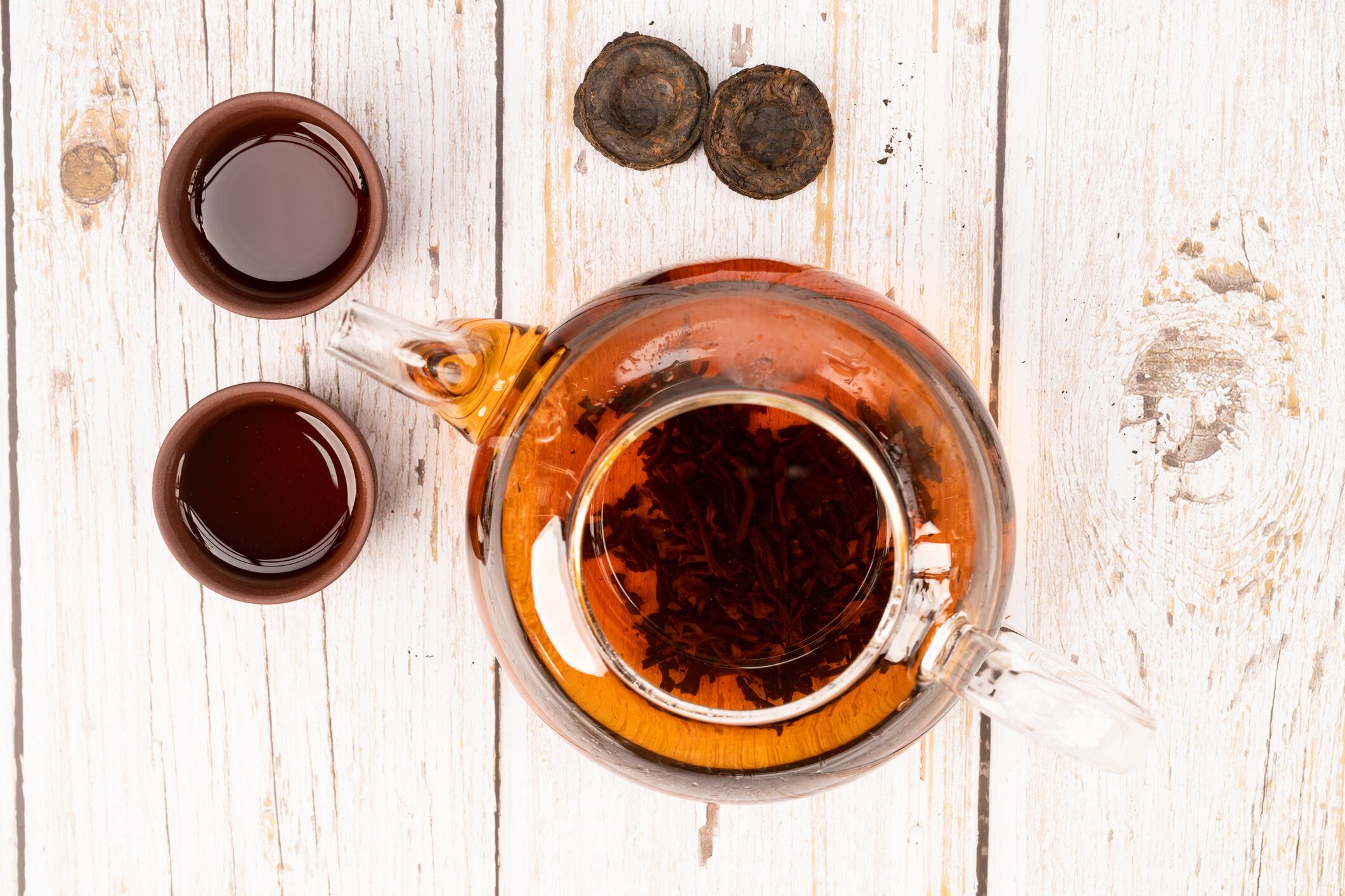 Pu-erh tea in glass pot and clay cups with tea bricks on wooden table