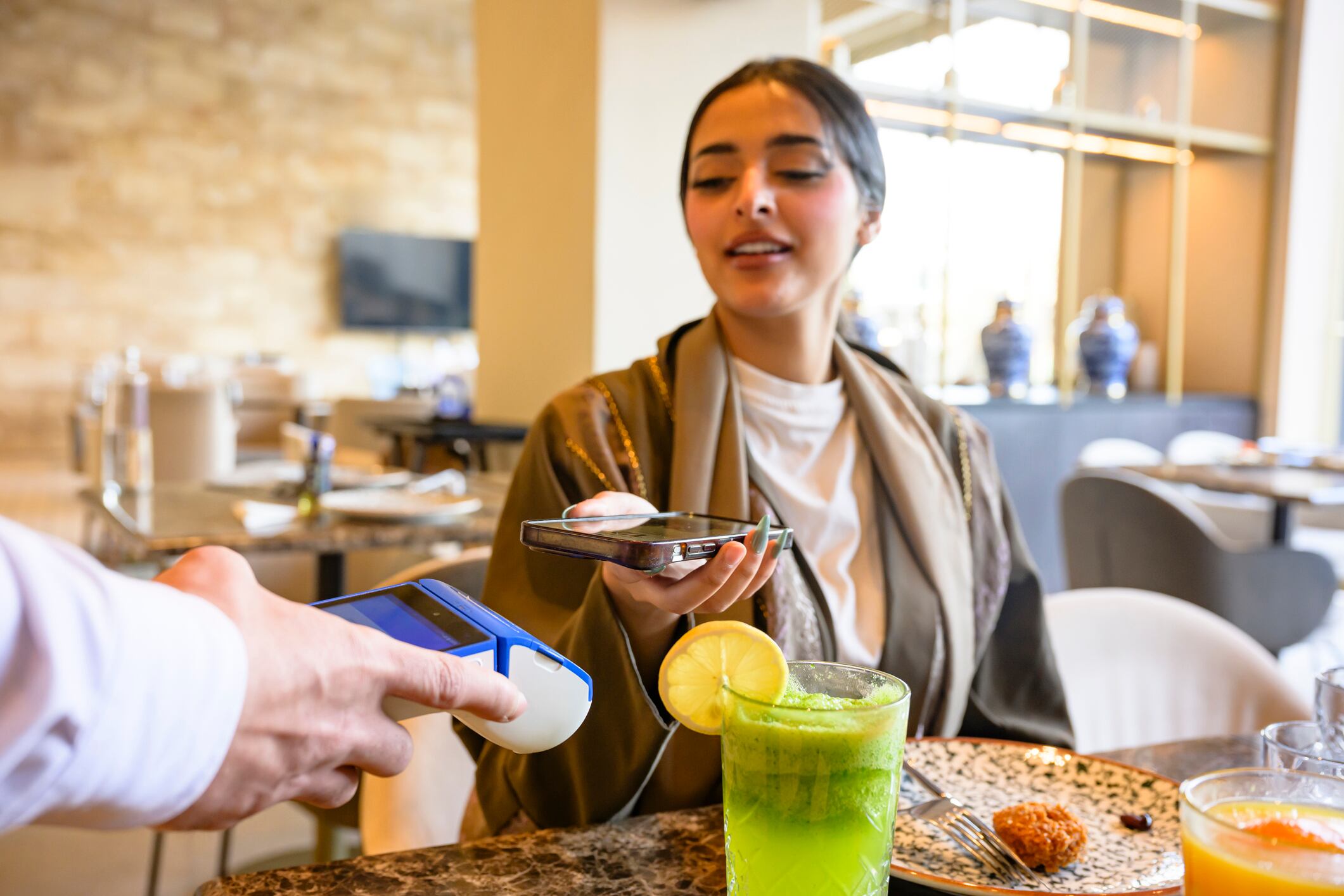 Woman tapping smartphone for contactless digital payment at a restaurant table.