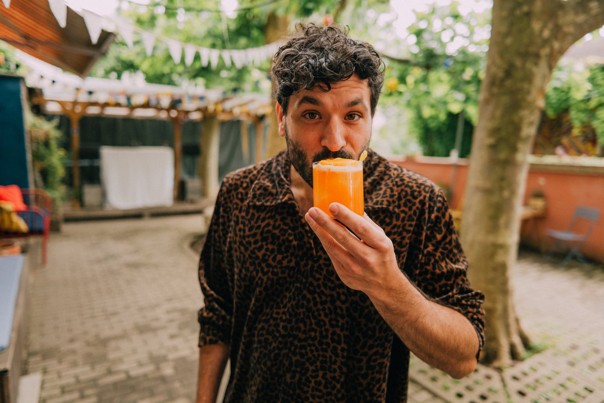 A man in a casual outdoor space holds a refreshing orange drink, celebrating leisure and everyday life. Part of a series with video