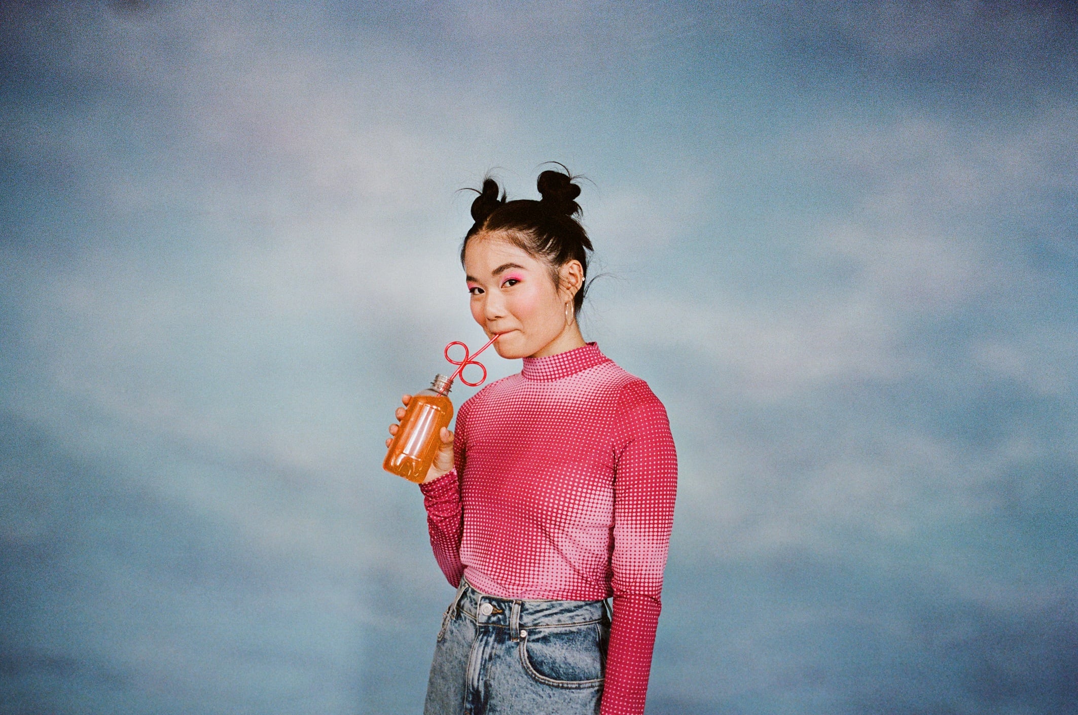 Portrait of young woman drinking juice from bottle while standing against colored background