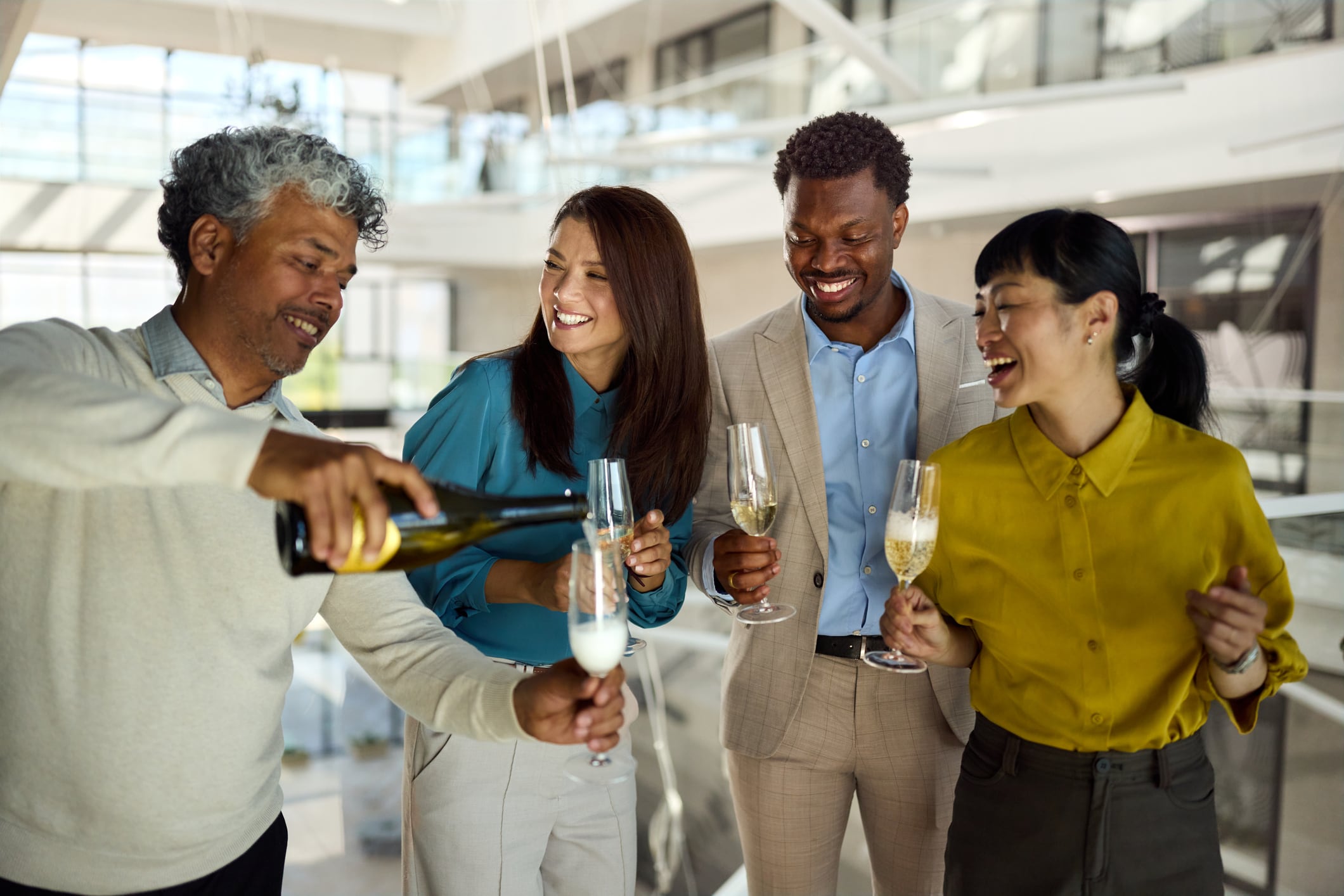 Happy Cuban entrepreneur pouring champagne to his colleagues on a party in a hallway of an office building.