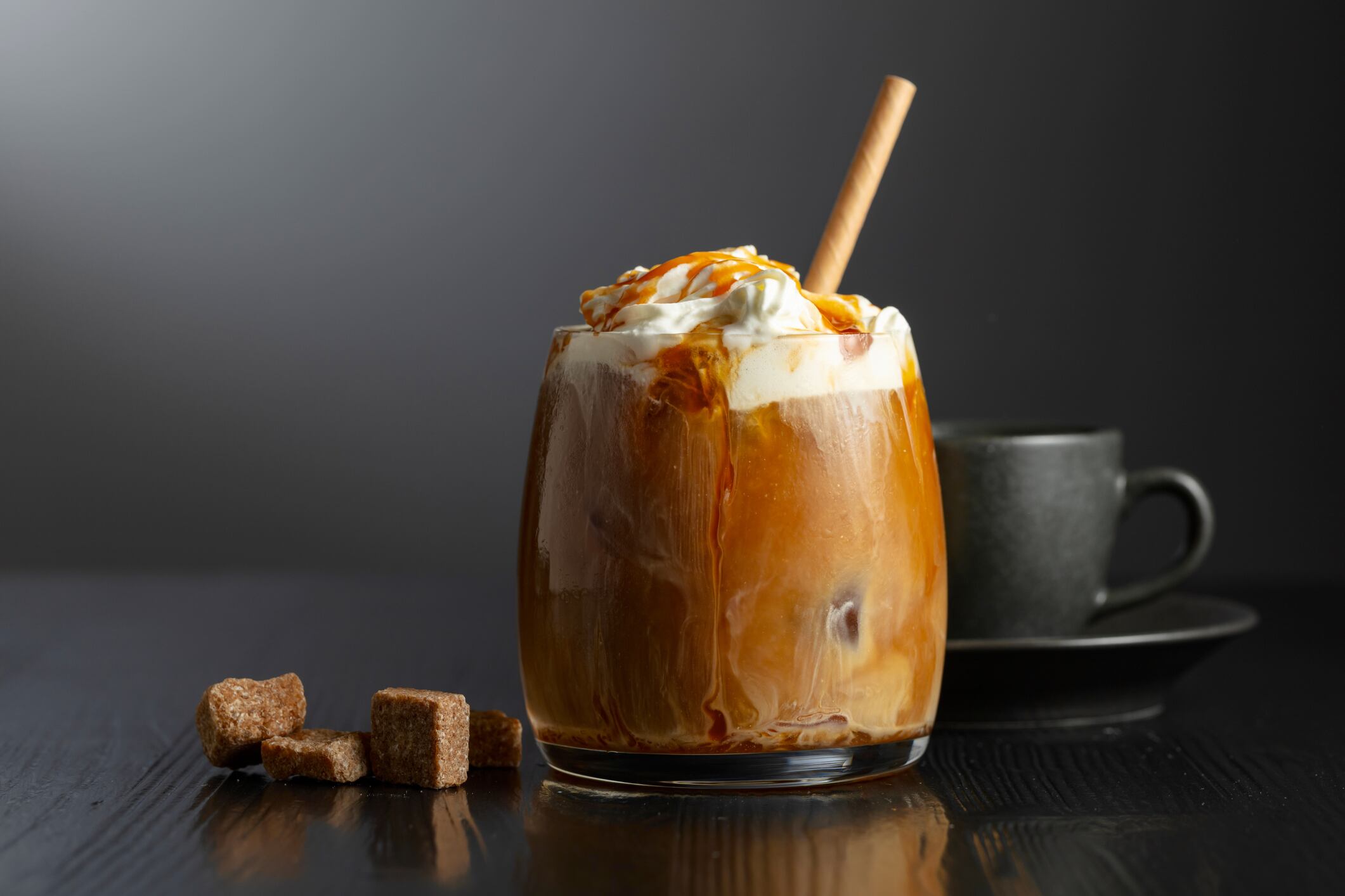 Iced coffee with whipped cream and caramel sauce and cup of black coffee on a black wooden table.